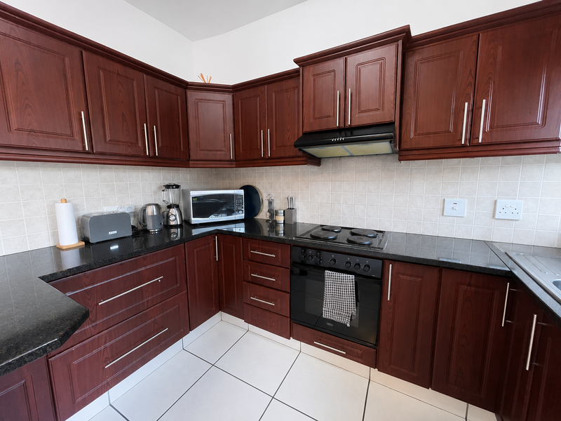 A functional kitchen featuring dark wood cabinetry, granite countertops, a tiled backsplash, and integrated appliances including an oven and hob.