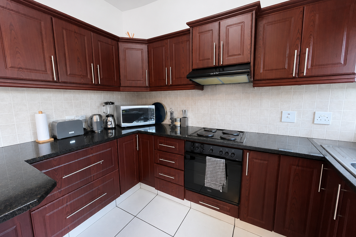 A functional kitchen featuring dark wood cabinetry, granite countertops, a tiled backsplash, and integrated appliances including an oven and hob.