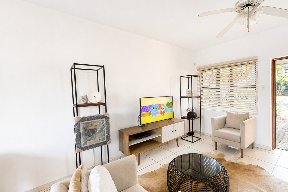 A bright living room featuring tiled flooring, a ceiling fan, and venetian blinds, with direct access to the exterior.
