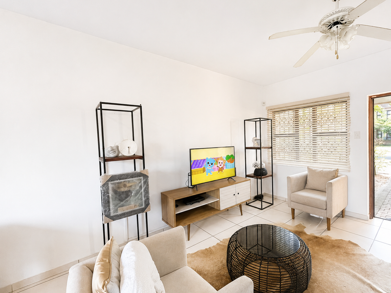 A bright living room featuring tiled flooring, a ceiling fan, and venetian blinds, with direct access to the exterior.
