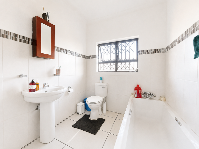 A functional bathroom featuring a pedestal basin, standard bathtub, and tiled finishes, complete with a security-gated window for natural light.