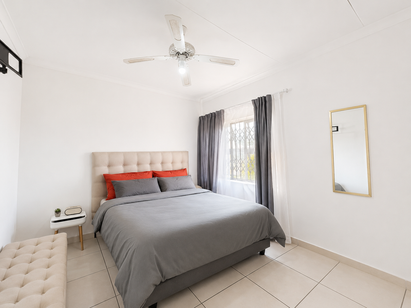 A bright and well-maintained bedroom featuring neutral tiled flooring, a ceiling fan, and a window fitted with a security gate.
