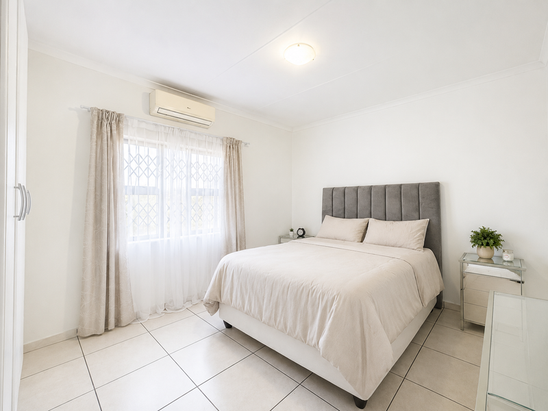 A well-maintained bedroom featuring tiled flooring, a built-in wardrobe, and a wall-mounted air conditioning unit.