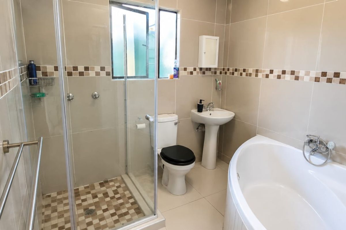 A well-maintained bathroom featuring a glass shower enclosure, a corner bathtub, a pedestal sink, and neutral wall tiling with a decorative mosaic border.