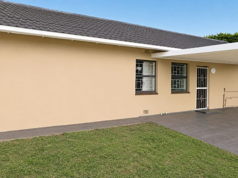 Rear view of the property featuring a paved patio area, covered carport, and well-maintained exterior walls with security features.