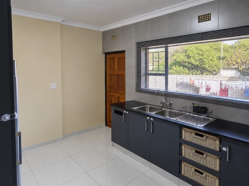 A functional kitchen featuring dark cabinetry, black stone countertops, a double sink, and tiled flooring with natural light from a large window.