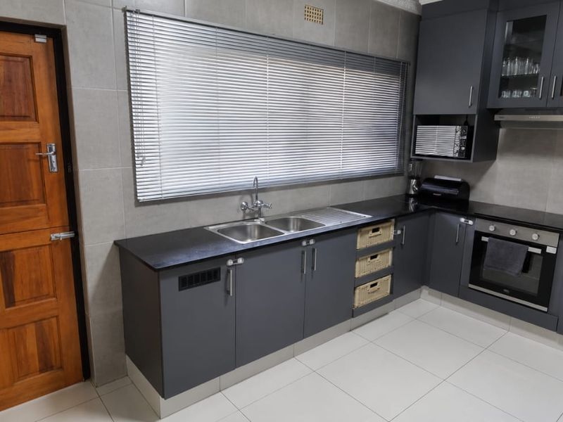 Modern kitchen featuring dark grey cabinetry, black countertops, built-in oven, extractor fan, double sink, and tiled finishes with a solid wood door.