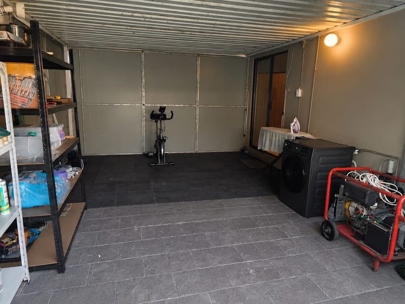 A functional garage space featuring tiled flooring, metal wall paneling, and exposed ceiling structure, currently utilized for storage and utility purposes.