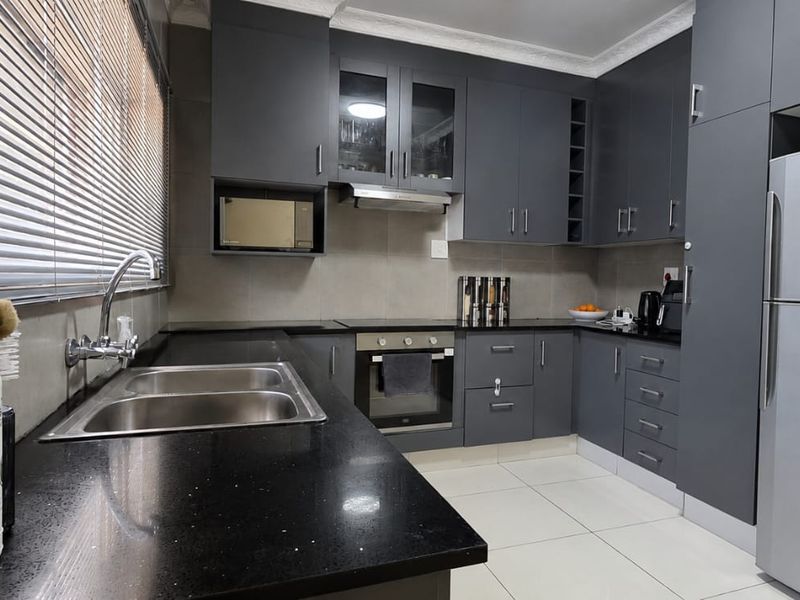 Modern kitchen featuring dark grey cabinetry, granite countertops, built-in oven, extractor fan, and tiled flooring.