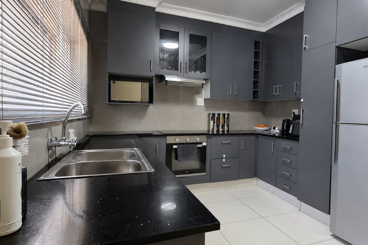 Modern kitchen featuring dark grey cabinetry, granite countertops, built-in oven, extractor fan, and tiled flooring.