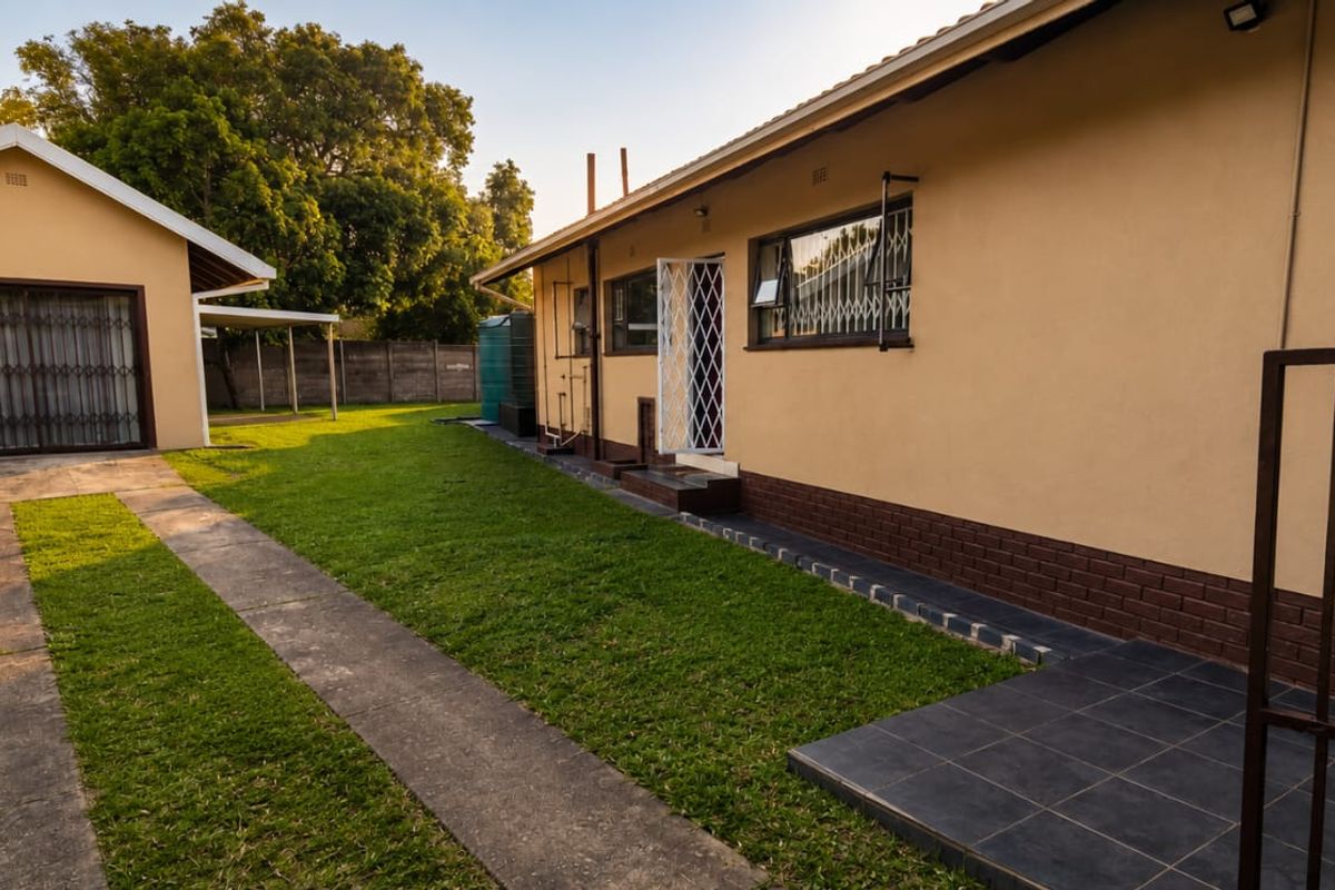 Rear view of the property featuring a well-maintained lawn, detached garage, paved driveway, and secure access points with security gates.