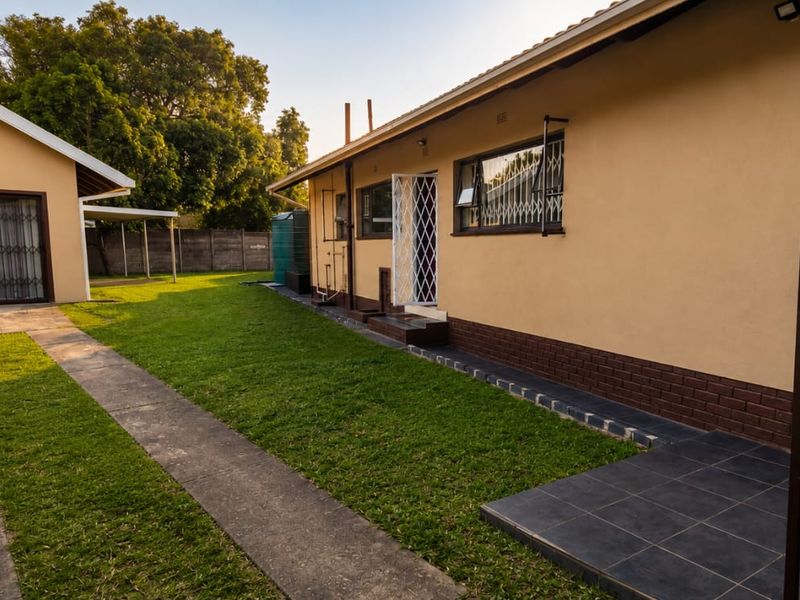 Rear view of the property featuring a well-maintained lawn, detached garage, paved driveway, and secure access points with security gates.