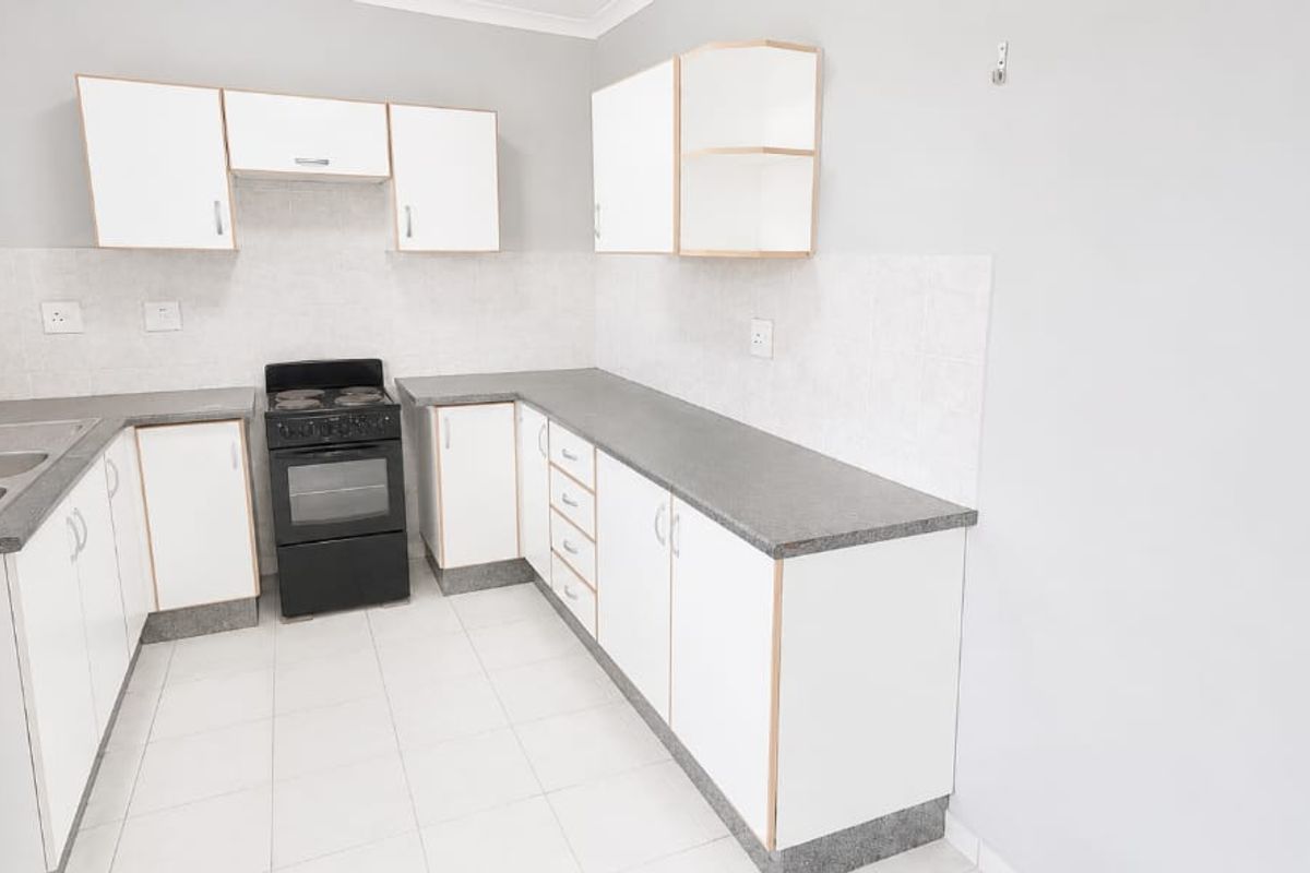 A clean, functional kitchen featuring white cabinetry, grey laminate countertops, a double basin sink, and a freestanding stove with tiled flooring and backsplash.