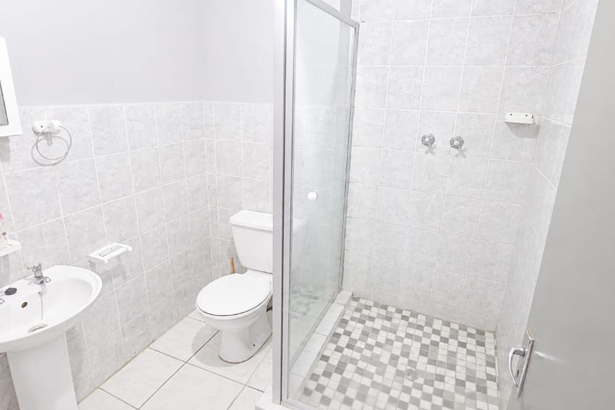 A functional bathroom featuring a pedestal basin, toilet, and a glass-enclosed shower with neutral wall and floor tiling.