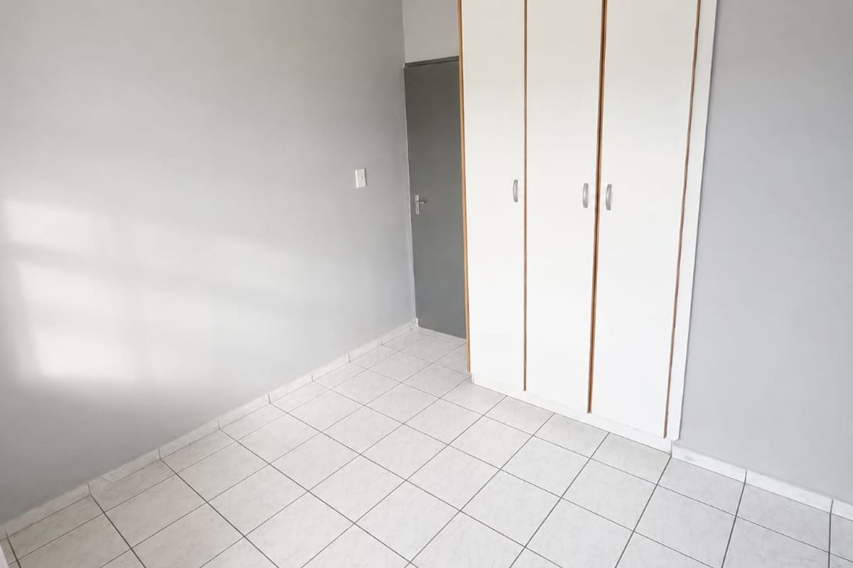 A clean, empty bedroom featuring neutral grey walls, white tiled flooring, and a built-in wardrobe with white doors.