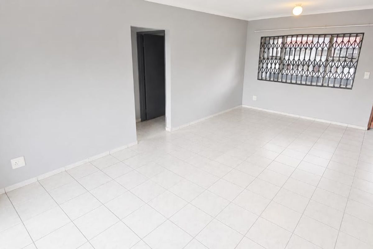 A bright, empty living area featuring neutral grey walls, tiled flooring, and a window fitted with a security gate.