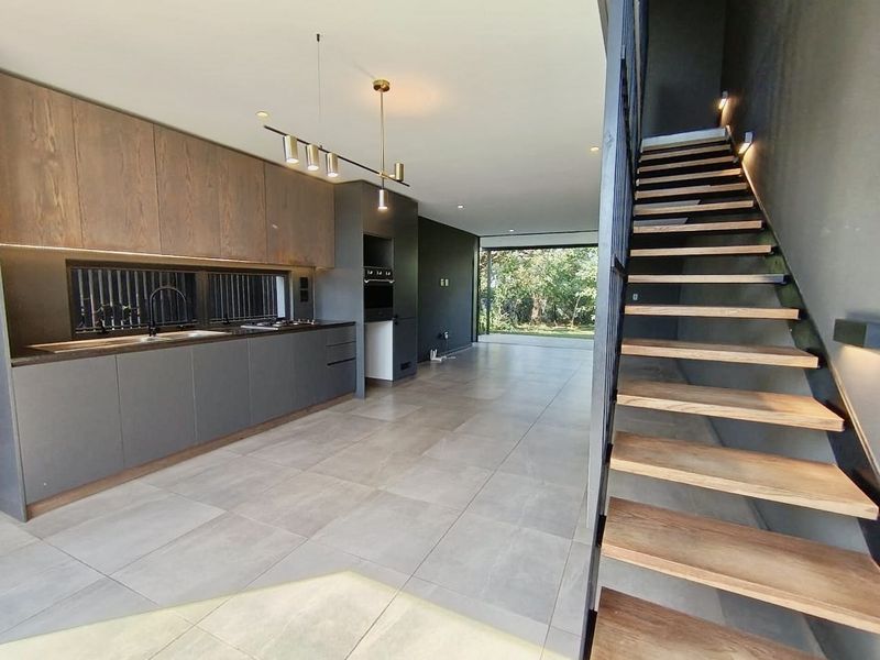 Modern open-plan kitchen and living area featuring sleek cabinetry, integrated appliances, large format floor tiles, and a contemporary floating staircase.