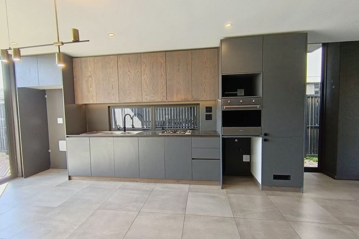 Modern kitchen featuring sleek grey and wood-tone cabinetry, integrated appliances, gas hob, and large format floor tiles in an open-plan layout.