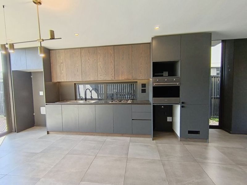 Modern kitchen featuring sleek grey and wood-tone cabinetry, integrated appliances, gas hob, and large format floor tiles in an open-plan layout.