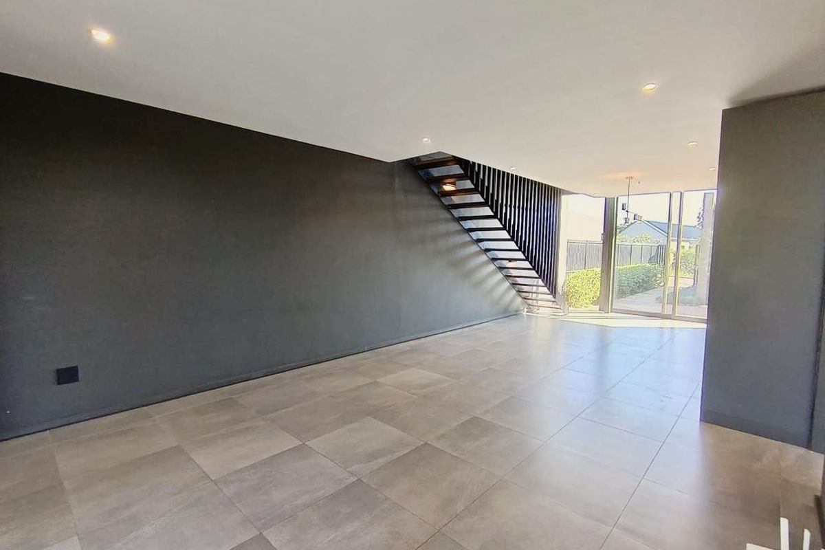 Spacious, modern open-plan living area featuring large format floor tiles, a contemporary staircase, and sliding glass doors leading to the exterior.