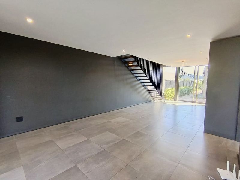 Spacious, modern open-plan living area featuring large format floor tiles, a contemporary staircase, and sliding glass doors leading to the exterior.