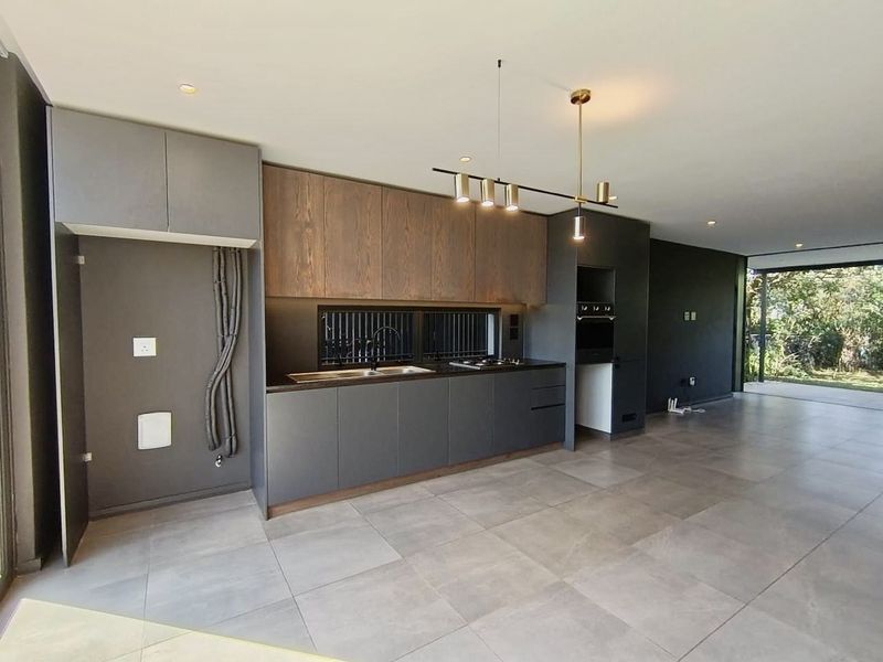 Modern open-plan kitchen featuring sleek dark cabinetry, wood-grain accents, integrated appliances, and large format floor tiles, flowing seamlessly into the living area.