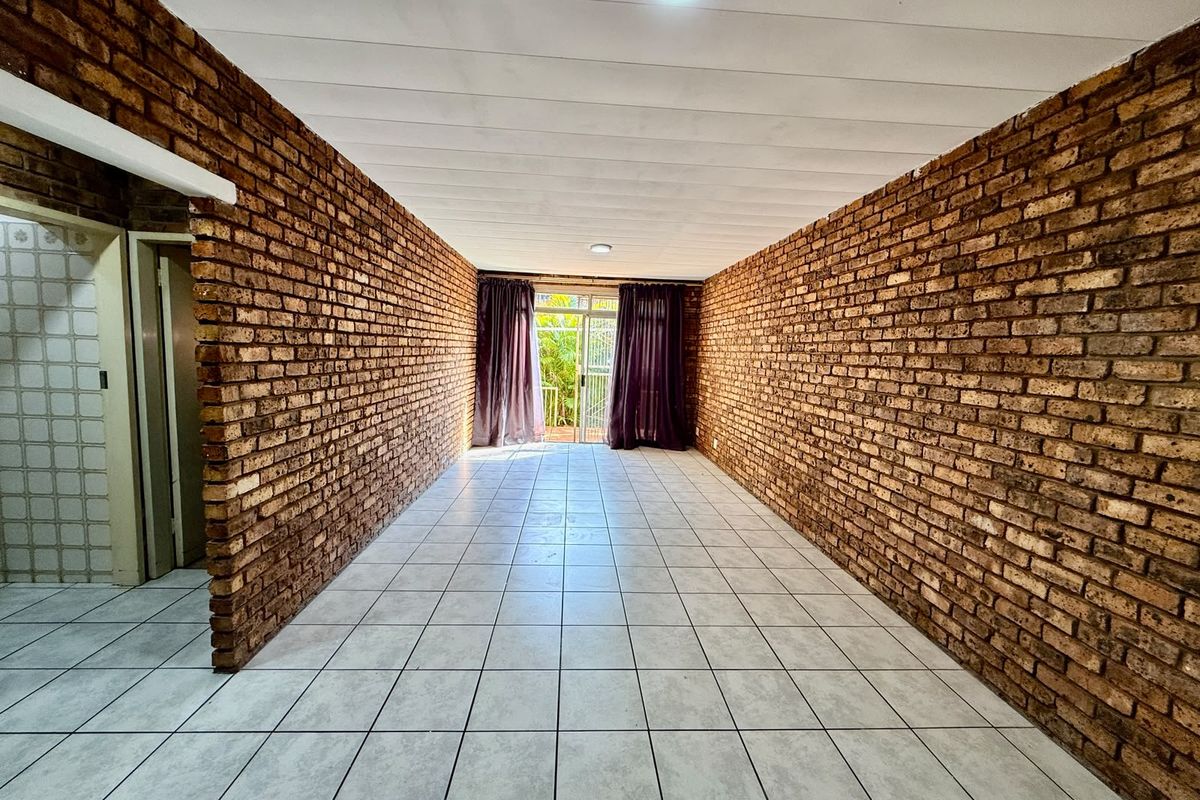 An empty, spacious living area featuring distinctive exposed brick walls, neutral ceramic floor tiles, and a sliding glass door leading to an outdoor space.