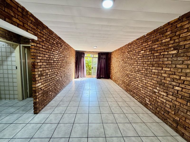 An empty, spacious living area featuring distinctive exposed brick walls, neutral ceramic floor tiles, and a sliding glass door leading to an outdoor space.