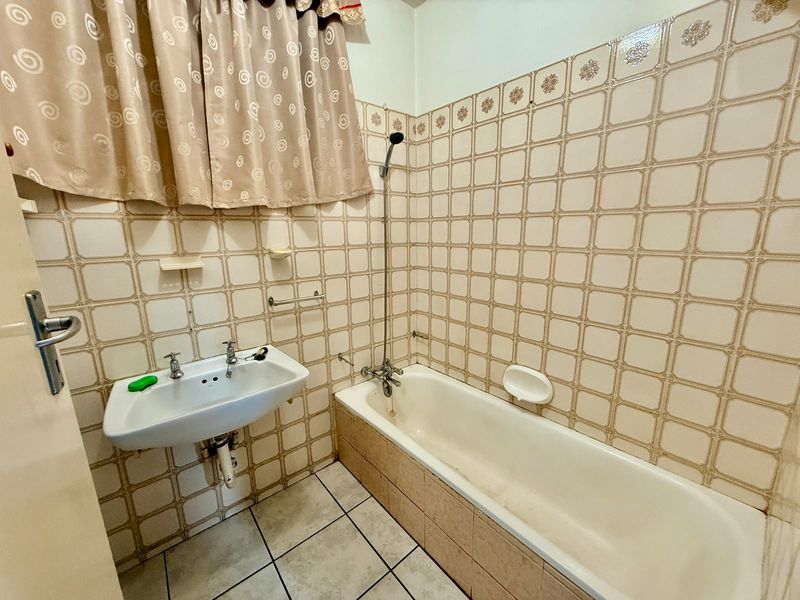 A dated bathroom featuring a wall-mounted basin, a standard bathtub with a handheld shower attachment, and traditional ceramic wall and floor tiling.