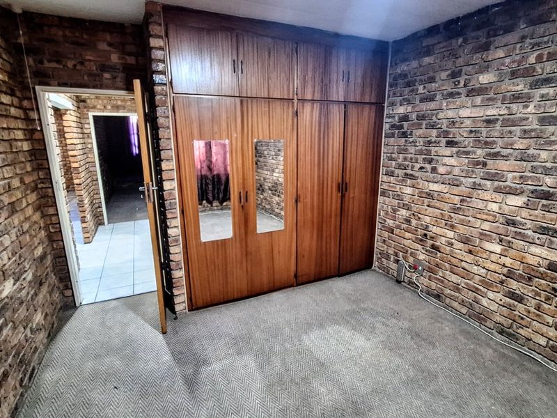 A bedroom featuring exposed brick walls, built-in wooden cupboards with integrated mirrors, and carpeted flooring.