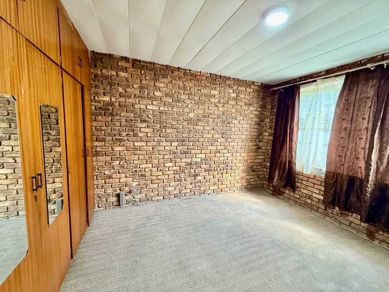 A bedroom featuring an exposed brick feature wall, built-in wooden cupboards, and carpeted flooring.