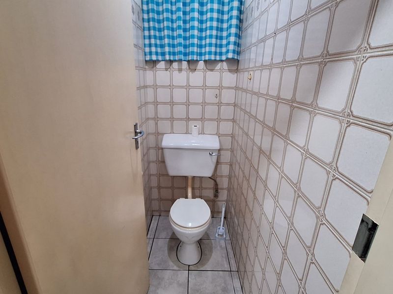 A compact, functional guest toilet featuring dated ceramic wall and floor tiles.
