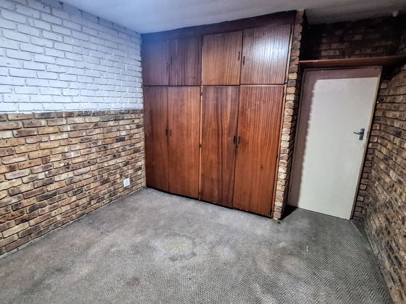 An empty bedroom featuring exposed brick walls, built-in wooden cupboards, and carpeted flooring, offering a blank canvas for renovation.