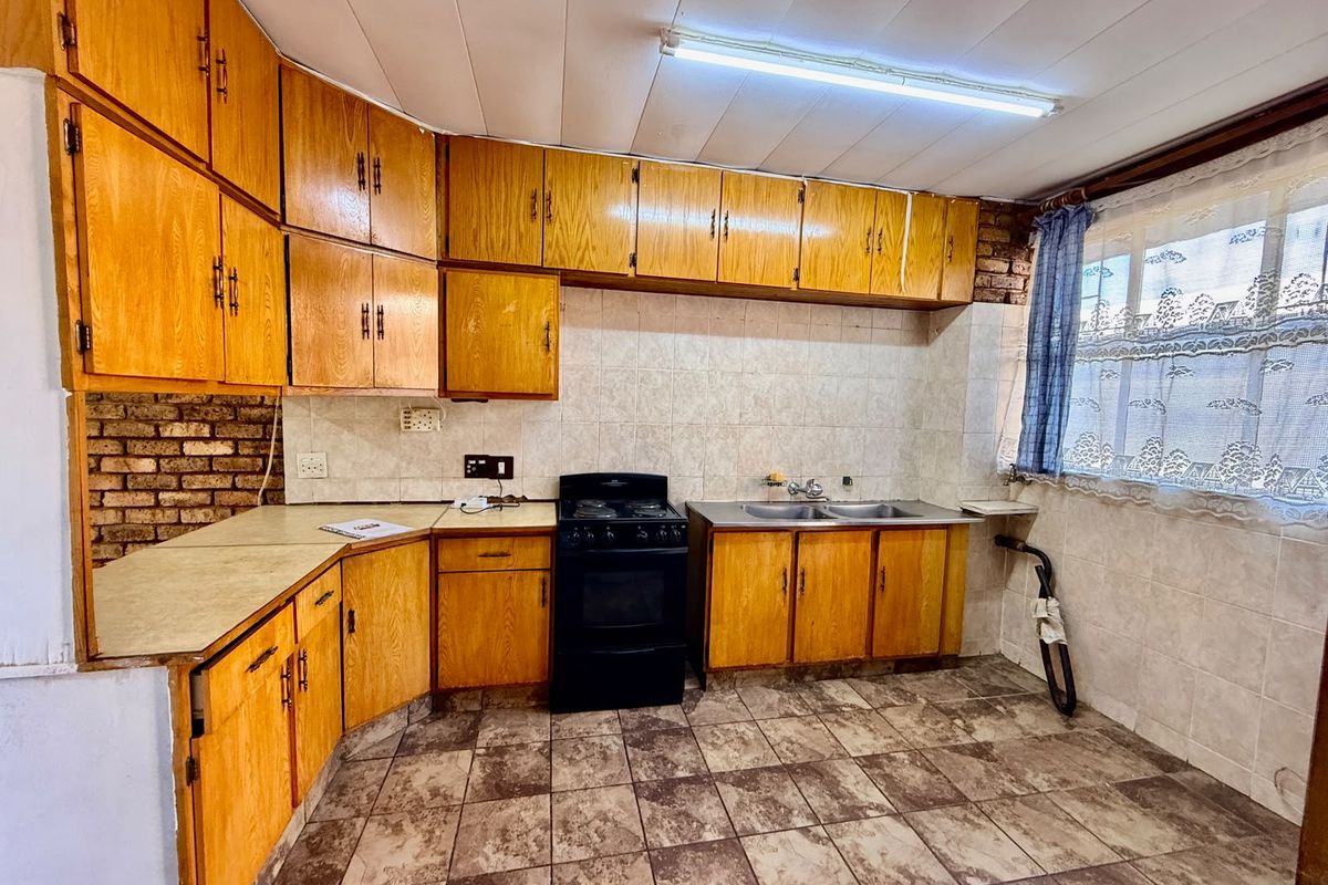 A dated kitchen featuring wooden cabinetry, laminate countertops, a double basin sink, and a freestanding stove, with tiled flooring and backsplash throughout.