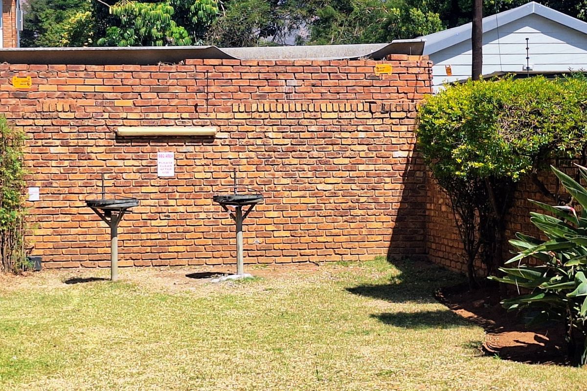 A rear outdoor area featuring a brick boundary wall and two built-in braai stands set within a grassed garden space.