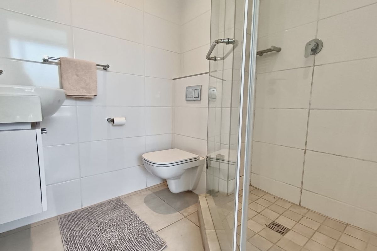 A functional bathroom featuring a wall-mounted toilet, vanity basin, and a glass-enclosed shower with tiled finishes.