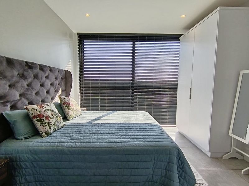 A well-maintained bedroom featuring tiled flooring, recessed downlighting, a large window with venetian blinds, and a modern built-in wardrobe.