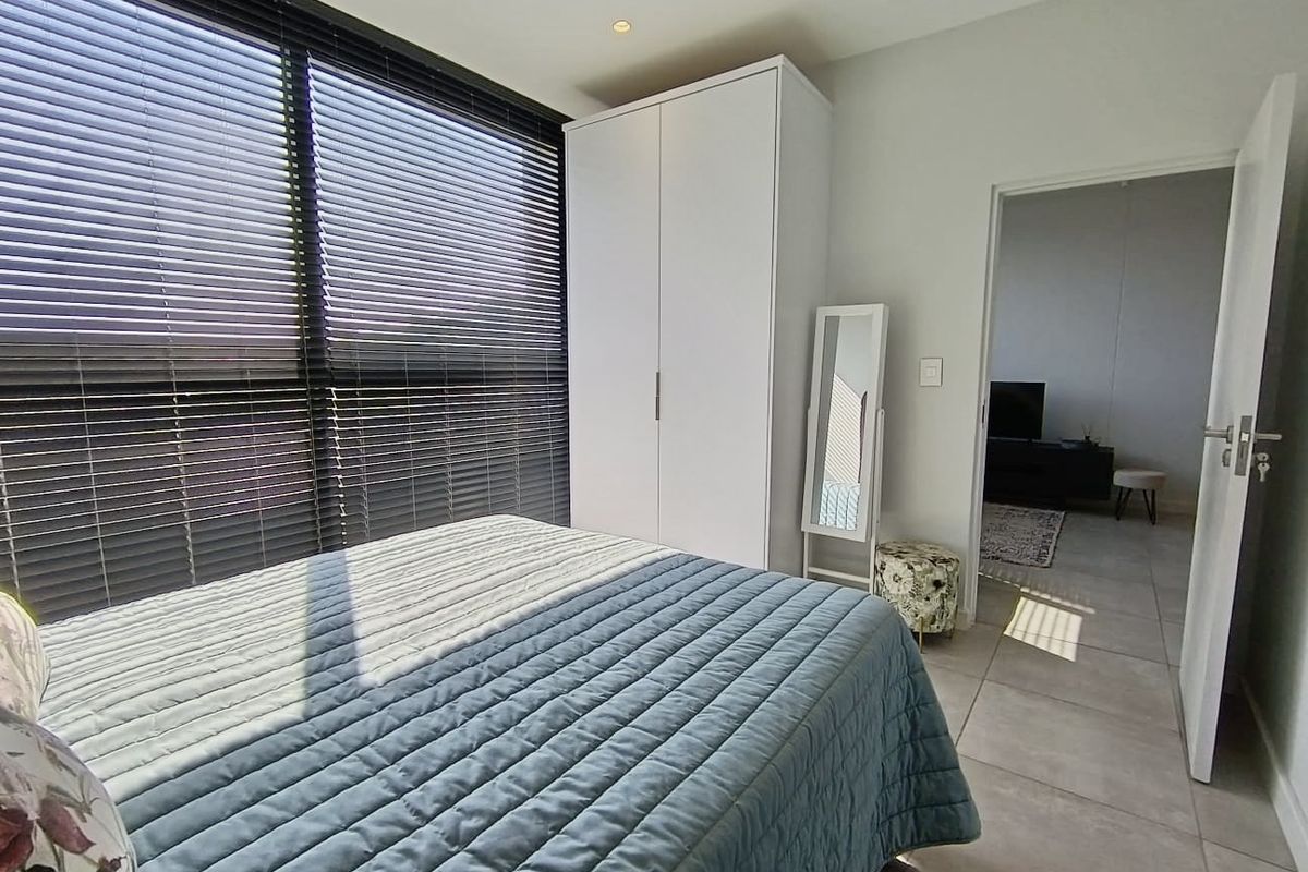 A bright bedroom featuring tiled flooring, a built-in wardrobe, and large windows fitted with venetian blinds, offering a clean and modern aesthetic.