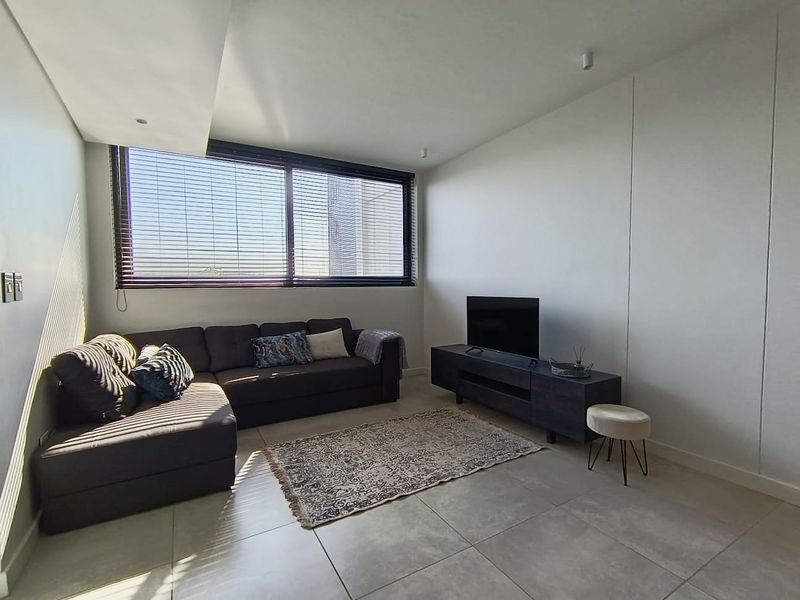A bright and modern living room featuring large windows with blinds, recessed ceiling lighting, and neutral tiled flooring.