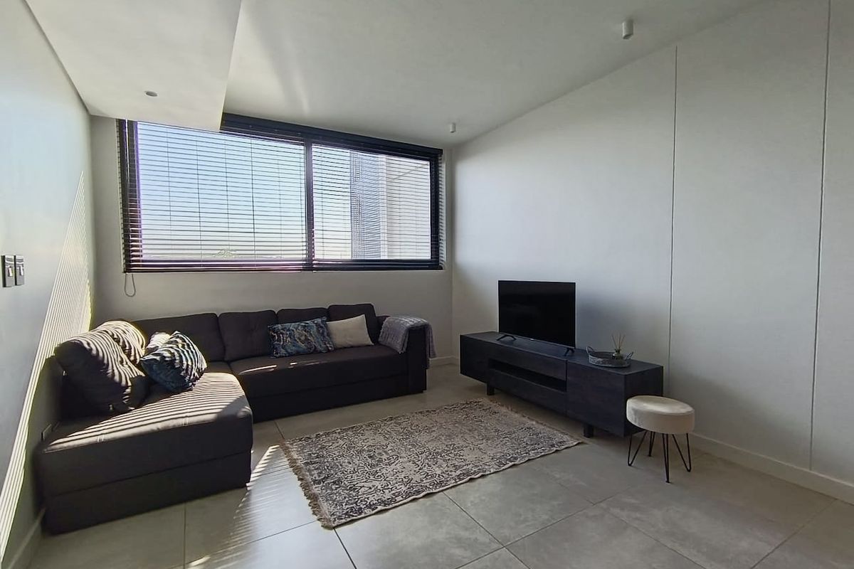 A bright and modern living room featuring large windows with blinds, recessed ceiling lighting, and neutral tiled flooring.