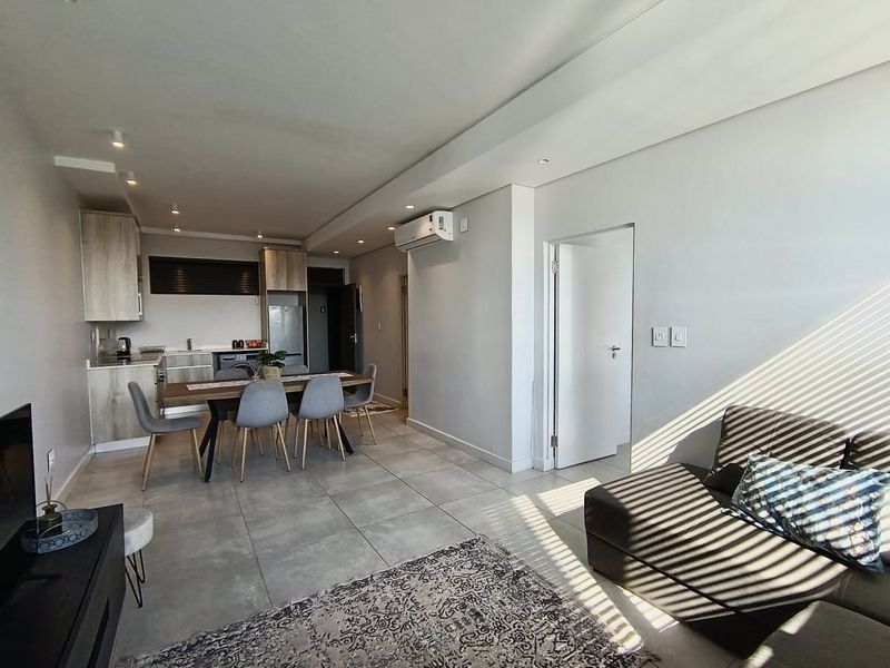 Modern open-plan living area featuring tiled floors, recessed lighting, and a sleek kitchen with built-in cabinetry and integrated appliances.