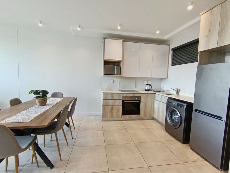 Modern open-plan kitchen and dining area featuring contemporary cabinetry, integrated appliances, tiled flooring, and recessed lighting in a well-maintained apartment setting.