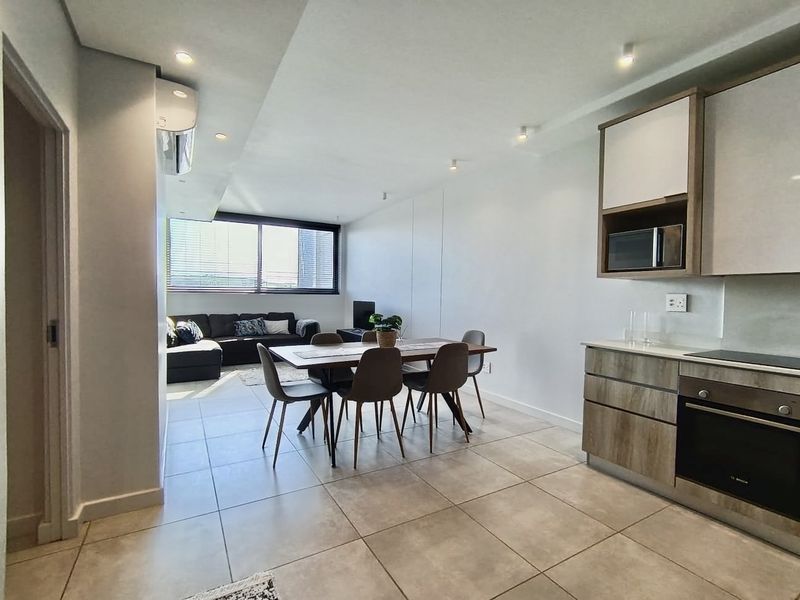 Modern open-plan living area featuring a contemporary kitchen with built-in appliances, tiled flooring, and recessed lighting, creating a bright and functional space.