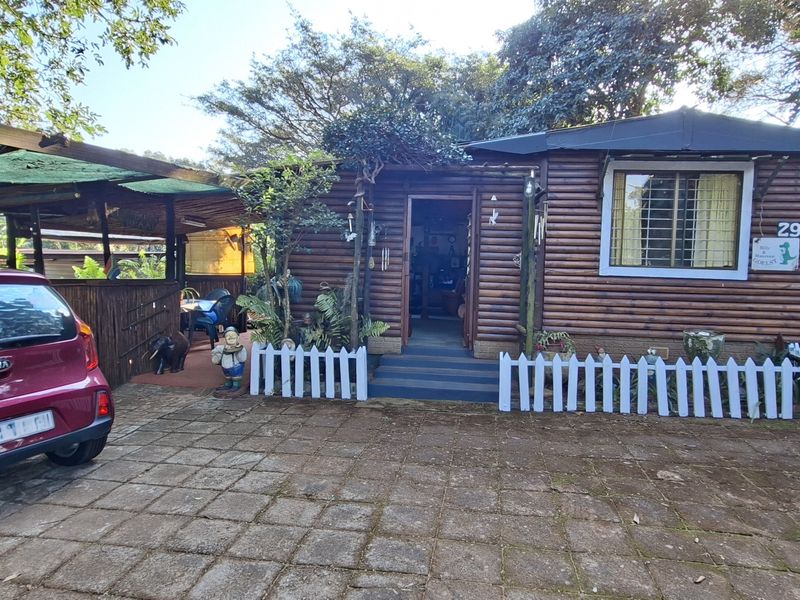 Front view of a log cabin style home featuring a paved driveway, covered carport area, and established garden surroundings.