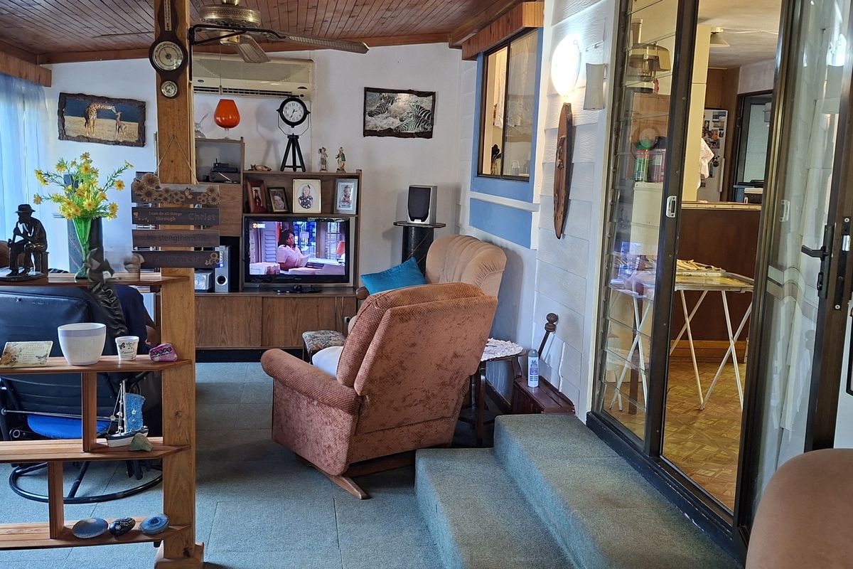 A living room featuring a timber-paneled ceiling, ceiling fan, and sliding glass doors leading to an adjacent area, with dated finishes throughout.