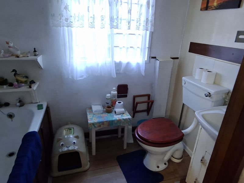 A compact, dated bathroom featuring a standard bathtub, pedestal basin, and toilet, requiring modernization of finishes and fixtures.