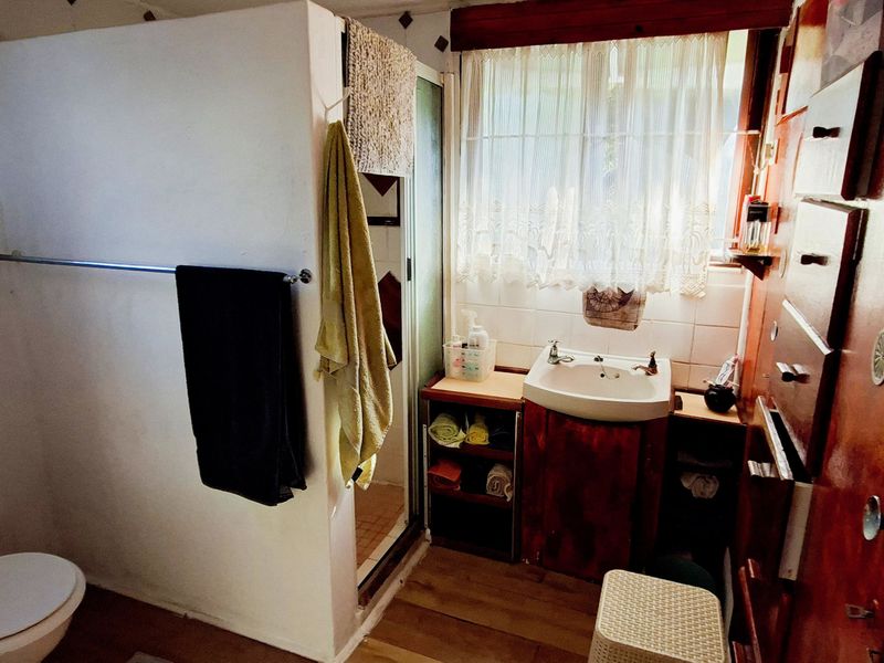 A compact bathroom featuring a toilet, vanity basin, and shower enclosure with dated cabinetry and finishes.