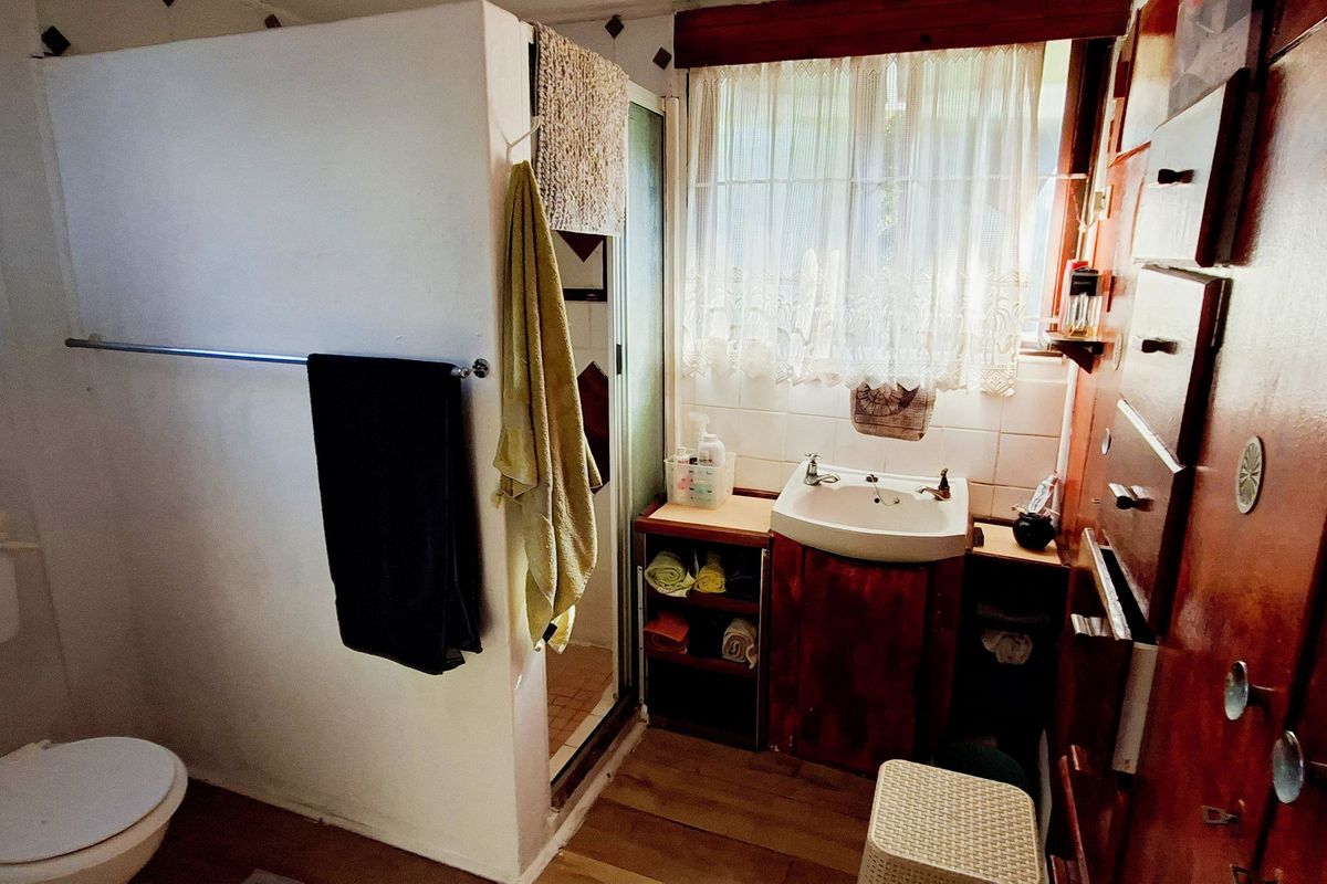 A compact bathroom featuring a toilet, vanity basin, and shower enclosure with dated cabinetry and finishes.