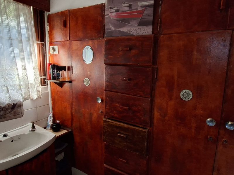 A bathroom featuring dated built-in wooden cabinetry with integrated storage and a ceramic washbasin with tiled splashback.