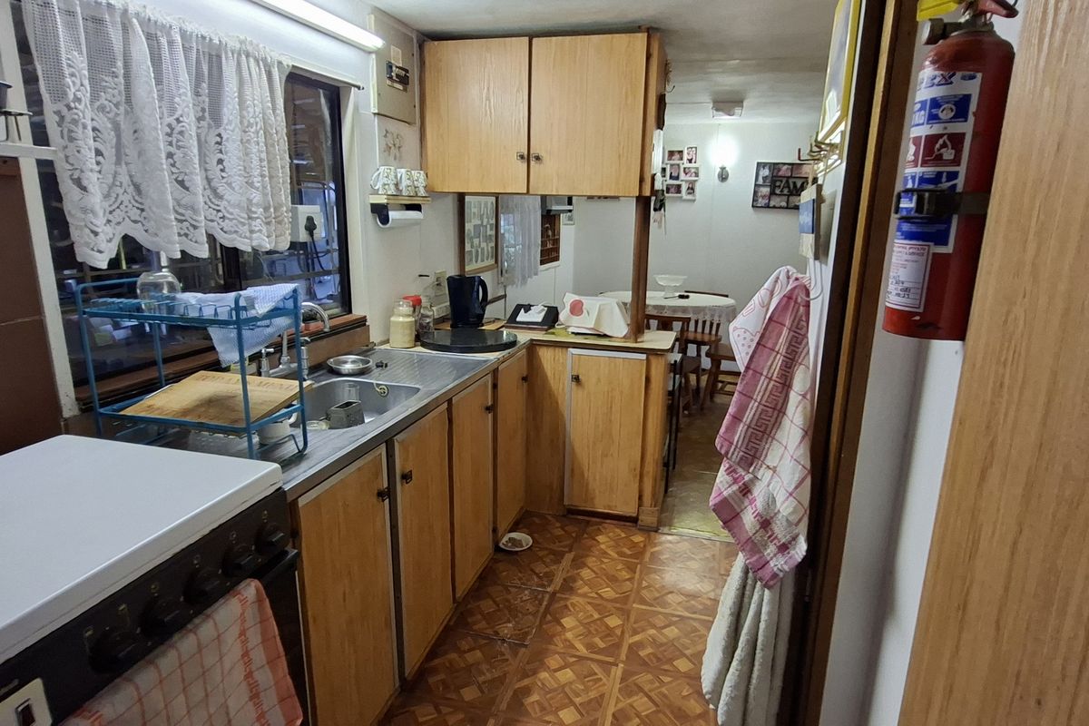 A compact, dated kitchen featuring laminate cabinetry, a stainless steel sink, and a freestanding stove, offering potential for a modern renovation.